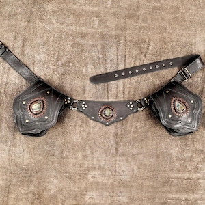 May include: A dark brown leather utility belt featuring two structured pouches and a central decorative panel. Each pouch and the centre piece are adorned with a teardrop or circular iridescent stone, metallic studs, and antique brass-toned hardware.