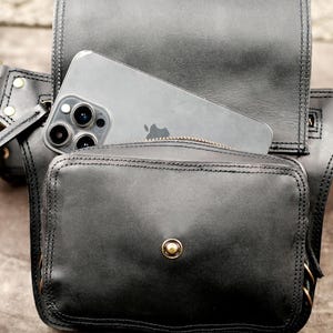 Open black leather festival hip pack holding smartphone inside main compartment to show phone size fit and magnetic snap closure.