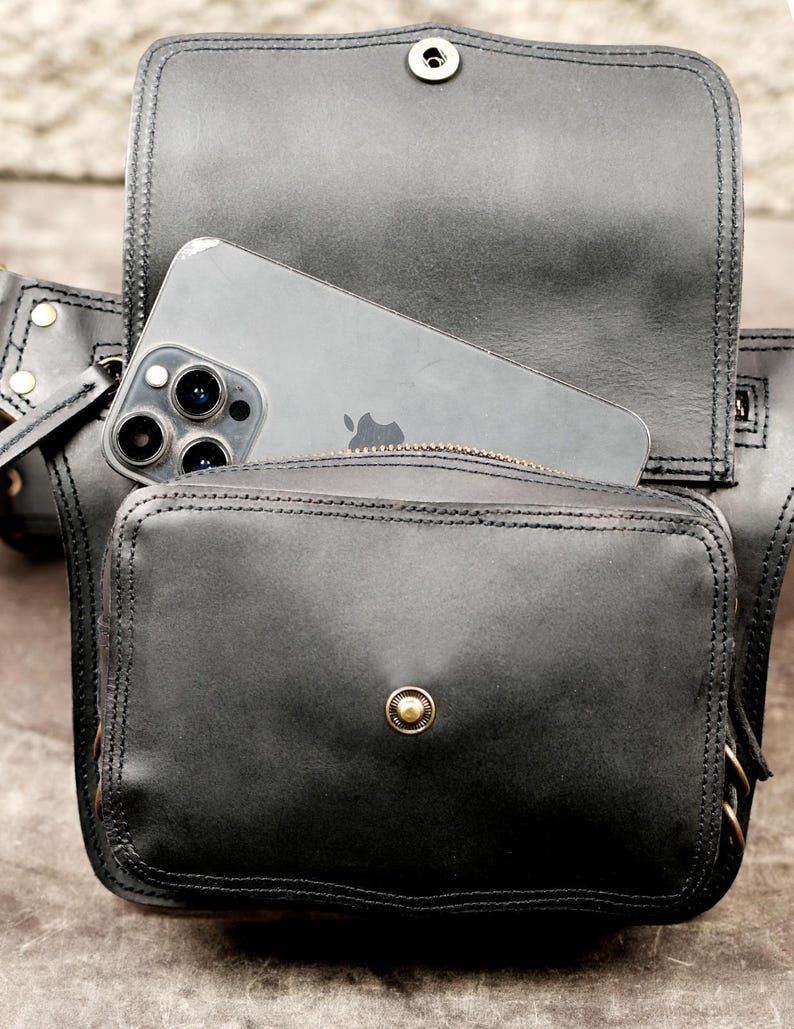Open black leather festival hip pack holding smartphone inside main compartment to show phone size fit and magnetic snap closure.