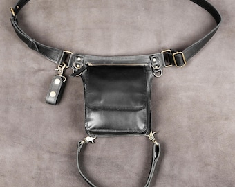 May include: A black leather drop leg bag featuring a main compartment with a flap closure, a zippered pocket, and an adjustable waist belt. The bag includes a secondary leg strap attached with metal swivel clips and brass-toned hardware accents.