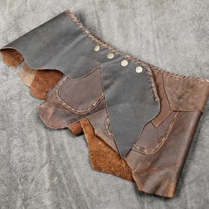 Könnte beinhalten: Ein Wickelaccessoire aus braunem Leder mit geschichteten Paneelen in verschiedenen Brauntönen. Das Stück ist mit sichtbaren Überwendlichstichen an den Kanten versehen und wird mit vier metallischen Druckknöpfen in einer diagonalen Reihe geschlossen.