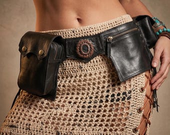 May include: A black leather utility belt featuring two attached pouches, a central circular braided brown leather accent, and metallic snap closures. The belt is worn over a beige crocheted skirt with side lacing and metal eyelet details.