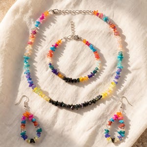 May include: A jewelry set consisting of a necklace, a bracelet, and two teardrop-shaped earrings. Each piece is crafted from small, multi-colored chip stones in shades of red, orange, yellow, green, blue, purple, and black, with silver-tone metal findings.