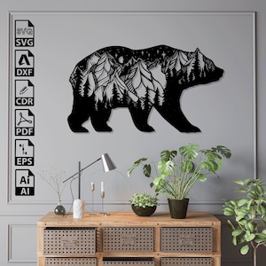 以下が含まれることがあります： 黒い金属製の壁飾りで、熊のシルエットの中に山脈が描かれています。熊は右を向いており、山脈は木々や星で詳細に描かれています。このアートは灰色の壁に掛けられており、その下に木の棚があります。