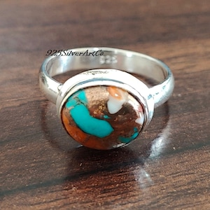 May include: A silver ring with a round turquoise and copper stone. The stone has a mix of blue, orange, and white colors.