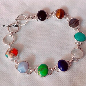 May include: A silver bracelet with a variety of colorful gemstones, including turquoise, green, blue, red, and brown. The bracelet has a toggle clasp.
