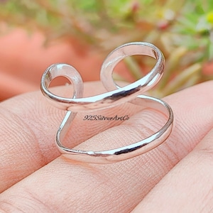 May include: A silver ring with a double band design. The ring is open and can be adjusted to fit different finger sizes. The ring is made of 925 sterling silver.