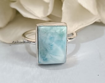 May include: A silver ring with a light blue, rectangular,  cabochon gemstone. The gemstone has a swirling, cloudy pattern.