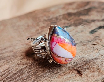 Puede incluir: Un anillo de plata con una piedra preciosa en forma de lágrima. La piedra preciosa es una mezcla de colores rosa, naranja, blanco y azul.