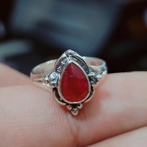 May include: A silver ring with a teardrop-shaped red gemstone set in a detailed silver setting.