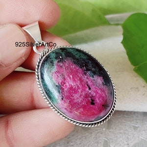 May include: A silver pendant with a green and pink oval gemstone. The pendant is set in a silver bezel with a rope edge. The text "925SilverArtCo" is visible on the pendant.