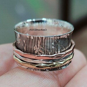 May include: A silver, gold, and copper spinning ring with a textured design and the text "925SilverArtCo".