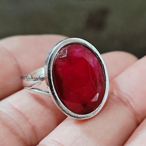 May include: A silver ring with a large, oval-shaped, red gemstone set in a bezel setting.