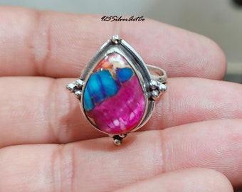 Puede incluir: Un anillo en forma de lágrima con una piedra preciosa colorida engastada en plata de ley. La piedra preciosa es una mezcla de rosa, azul y blanco.