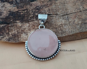 May include: A silver pendant with a round, pale pink gemstone. The pendant has a beaded border and a silver bail.