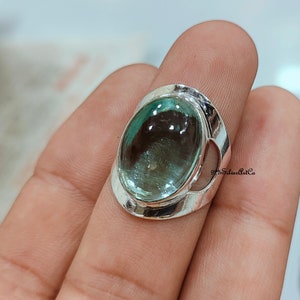 May include: A silver ring with a large oval-shaped aquamarine gemstone. The ring has a delicate, openwork design around the stone.