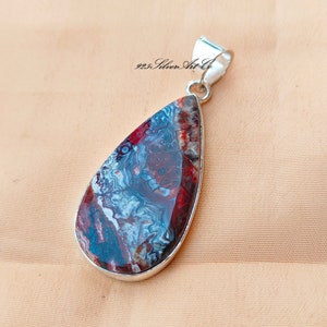 May include: A teardrop-shaped pendant with a red, blue, and white agate stone set in sterling silver. The pendant is approximately 2 inches long and features a bail for attaching a chain.