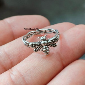 May include: A silver ring with a braided band and a bee design. The bee is detailed with wings, legs, and a stinger.