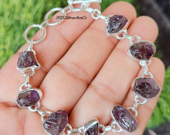 May include: A silver bracelet with a toggle clasp features seven purple amethyst gemstones. The bracelet is made with 925 sterling silver.