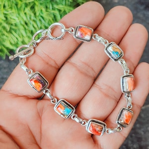 May include: A silver bracelet with a toggle clasp features a chain with square-shaped turquoise and orange stones.