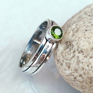 May include: A silver ring with a green gemstone set in the center. The ring is made of three bands that are stacked on top of each other.