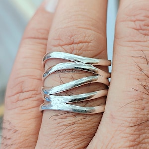 May include: A silver ring with a hammered finish and a wavy design. The ring is made of 925 sterling silver and is a statement piece.