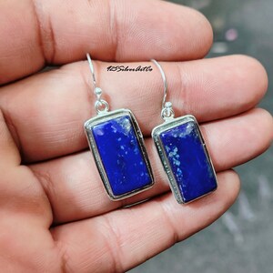 May include: A pair of silver earrings with rectangular blue lapis lazuli stones. The earrings have a simple design and are perfect for everyday wear.