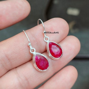 May include: A pair of silver dangle earrings with teardrop-shaped red ruby gemstones.