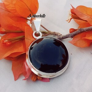 May include: A silver pendant with a black onyx stone. The pendant is round and has a smooth, polished finish. The stone is set in a silver bezel and the pendant has a bail for attaching to a chain.