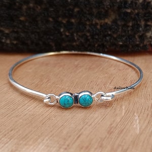 Op de afbeelding: Een zilveren armband met twee turquoise stenen. De armband heeft een eenvoudig ontwerp en is perfect voor dagelijks gebruik.