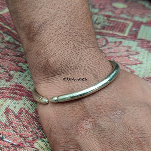 May include: A silver bangle bracelet with rounded ends. The bracelet is worn on a person's wrist.
