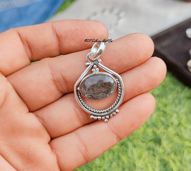 May include: Silver pendant with a clear quartz stone with black inclusions. The pendant is in the shape of a teardrop with a twisted silver bail.