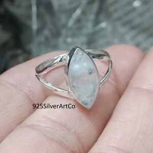 Könnte beinhalten: Ein silberner Ring mit einem markisenförmigen Mondstein. Der Ring hat ein zartes, offenes Design und der Stein ist in einer Zargenfassung gefasst. Der Text "925SilverArtCo" ist auf dem Ring sichtbar.