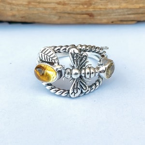 Può includere: Anello d'argento con un design a forma di ape e due pietre preziose gialle. L'ape è dettagliata e ha le ali. L'anello è attorcigliato e ha un design a corda.