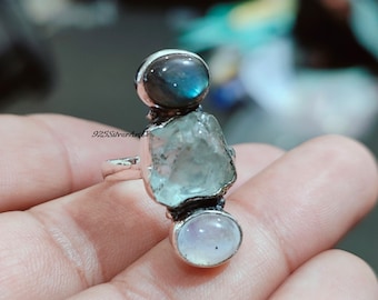 May include: Silver ring with three stones: a blue labradorite, a clear aquamarine, and a white moonstone.