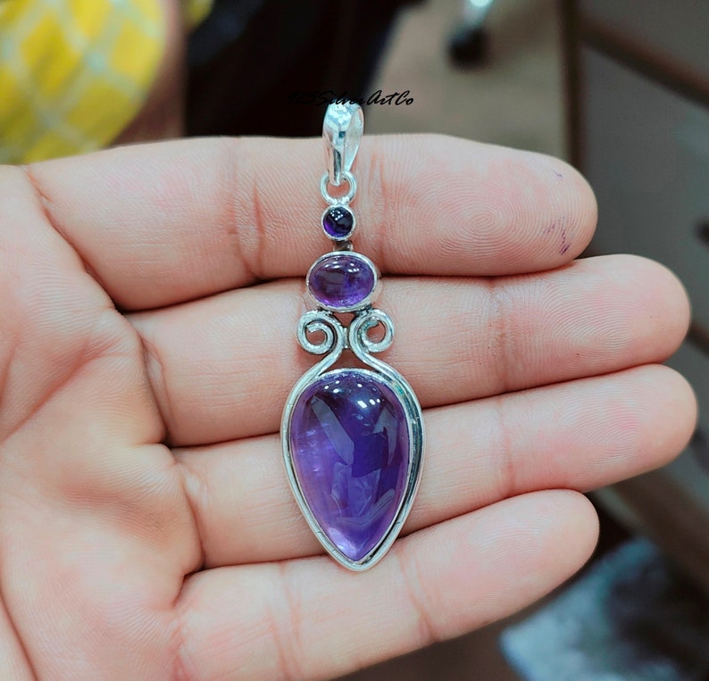 May include: A silver pendant with a teardrop-shaped amethyst gemstone. The pendant has a delicate design with two smaller amethyst gemstones above the main stone.