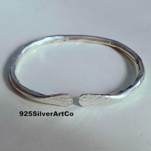 May include: A silver hammered bangle bracelet with a slightly open design. The bracelet is made of 925 sterling silver and is a simple, yet elegant piece of jewelry.