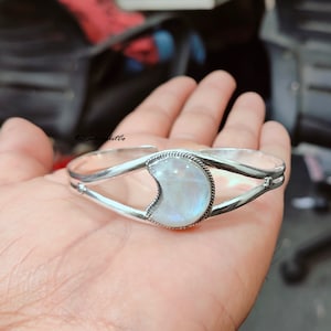 May include: A silver bracelet with a crescent moon shaped moonstone. The bracelet is open and adjustable.