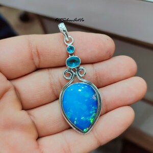 May include: A silver pendant with a blue opal gemstone and two smaller blue gemstones. The pendant has a delicate, ornate design.