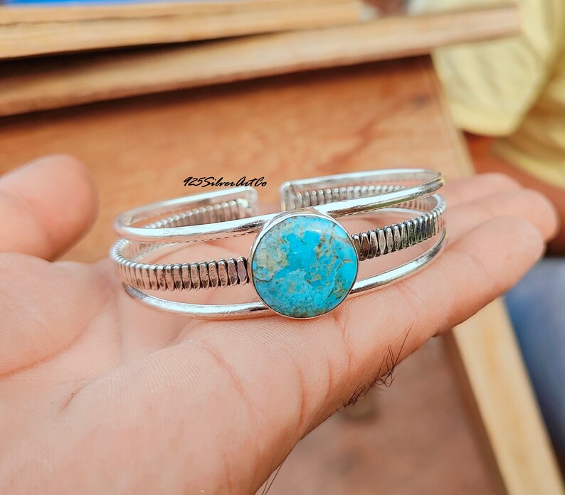 May include: A silver cuff bracelet with a turquoise stone set in the center. The bracelet has a textured design and three bands.