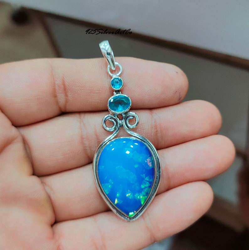 May include: A silver pendant with a teardrop-shaped blue opal gemstone and three smaller blue gemstones. The pendant is on a silver chain.