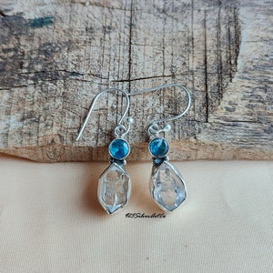 May include: A pair of silver dangle earrings with clear quartz crystal drops and blue topaz accents.