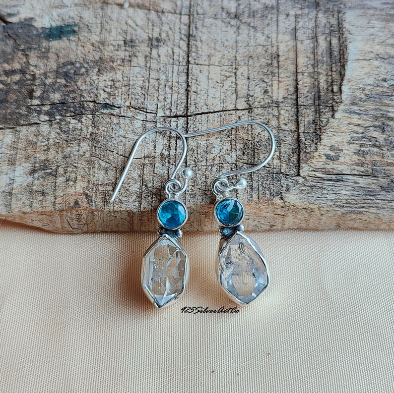 May include: A pair of silver dangle earrings with clear quartz crystal drops and blue topaz accents.