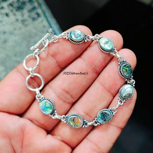 Puede incluir: Un brazalete de plata con cierre de palanca y detalles de concha de abulón de forma ovalada. El brazalete es 925 Silver Art Co.