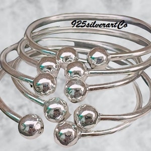May include: Five silver bangle bracelets with a ball design. The bracelets are stacked on top of each other. The text "925silverartCo" is engraved on the top bracelet.