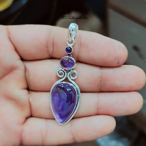 May include: A silver pendant with a large, teardrop-shaped amethyst gemstone. The pendant also features two smaller amethyst gemstones and intricate silver detailing.