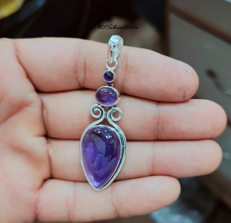May include: A silver pendant with a large, teardrop-shaped amethyst gemstone. The pendant also features two smaller amethyst gemstones and intricate silver detailing.