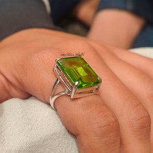 Puede incluir: Un anillo de plata con una gran piedra preciosa verde esmeralda. La piedra preciosa es rectangular y tiene un corte facetado.