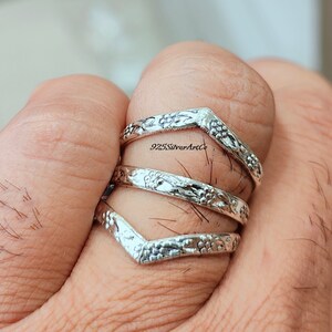 Op de afbeelding: Drie zilveren ringen met een chevron-ontwerp en bloemmotieven. De ringen zijn op een vinger gestapeld.