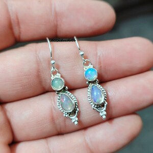 May include: A pair of silver earrings with opal gemstones. Each earring features a teardrop-shaped opal, a round opal, and a decorative silver setting. The earrings are displayed against a neutral background.